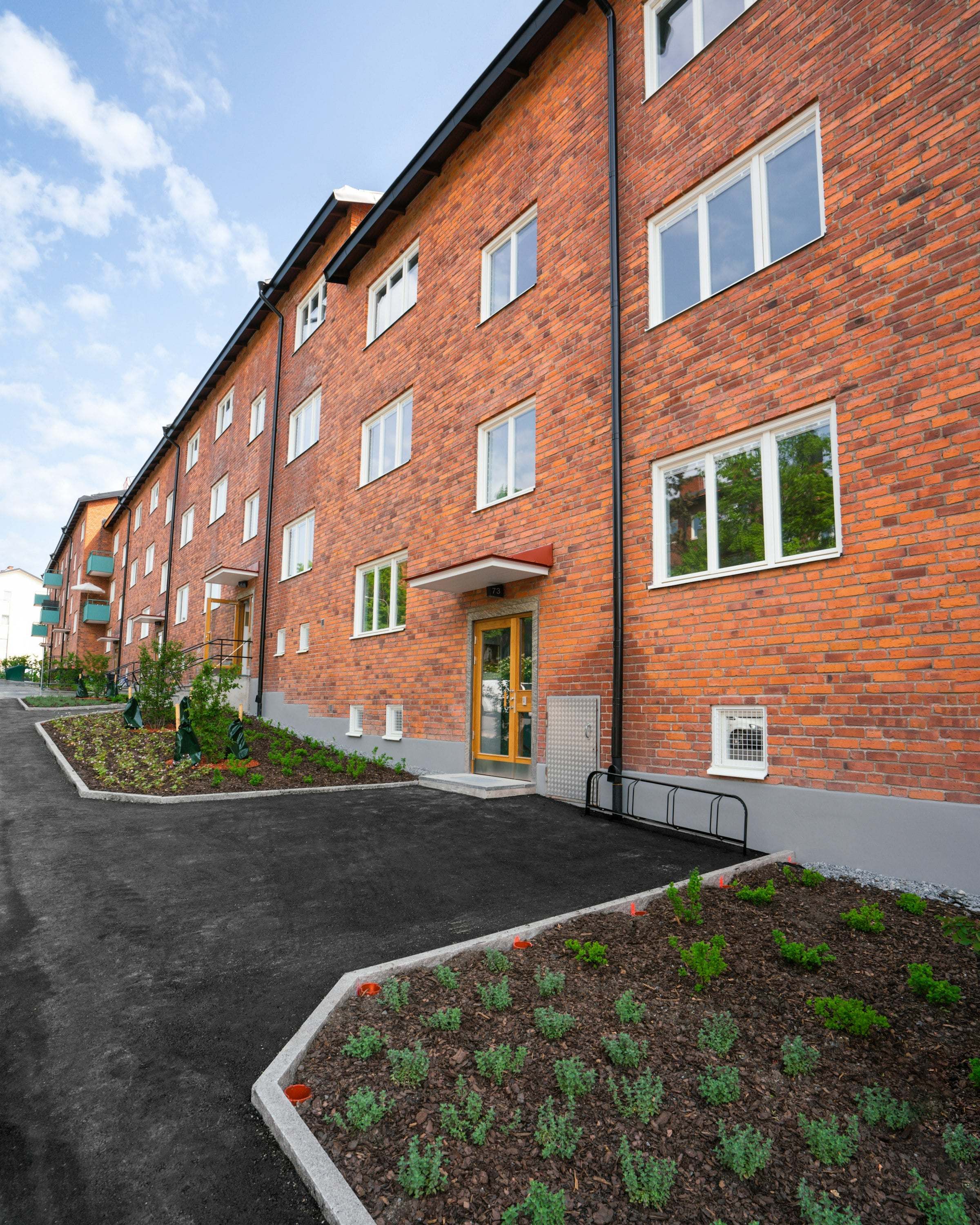 Flerbostadshus i rött tegel med nyplanterade rabatter framför entrén